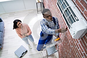 Woman Looking At Technician Repairing Air Conditioner