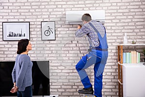 Woman Looking At Technician Repairing Air Conditioner