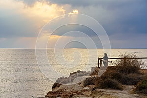 Woman looking to the horizon from a viewpoint at golden sunset over the sea.