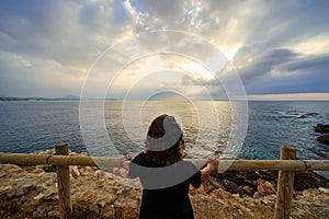 Woman looking to the horizon from a viewpoint at golden sunset over the sea.