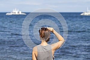 Woman looking to sea and white boat. Red hair tanned girl from back staring at the seascape