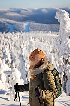 Woman looking to winter mountains from viewpoint during hiking in snowy forest