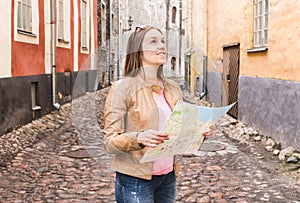 Woman looking up and holding map. Smiling traveler sightseeing.