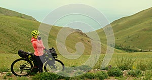 The woman looking at the view of beautiful lake by mountains. The girl rests beside her bike in mountains after her