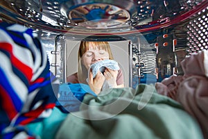 Woman looking into washing machine at laundromat with clothing. Woman removing laundry from top load washing machine