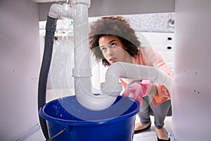 Woman Looking At Water Leaking From Sink Pipe