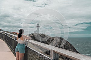 Woman looking at the white lighthouse at the coast of Byron Bay