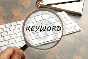 Woman looking at word Keyword and keyboard through magnifying glass