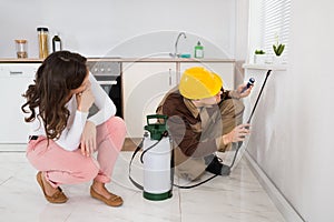 Woman Looking At Worker Spraying Insecticide Under Windowsill