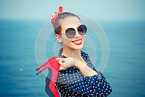 Woman looking at you, camera smiling holding red shoes