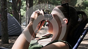 Woman Looks Through Binoculars on a Chaise Longue in a Forest near Camping