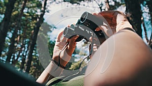 Woman Looks Through Binoculars on a Chaise Longue in a Forest near Camping