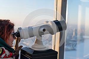 A woman looks through binoculars on the observation deck of a skyscraper