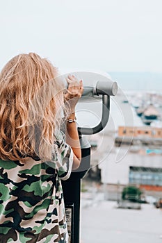 Woman looks through binoculars at the sea. Traveler vacation holiday concept. Using coin operated panoramic telescope