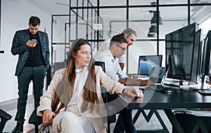 Woman looks into the camera. Team of stockbrokers works in modern office with many display screens photo