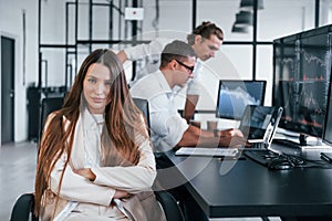 Woman looks into the camera. Team of stockbrokers works in modern office with many display screens