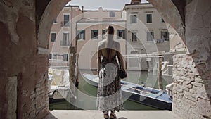 Woman looks at canal under arcades in Venice