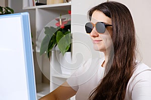 A woman looks at a computer screen through perforated glasses with holes to improve vision in astigmatism and