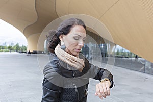 A woman looks at her watch. In the town. Brunette with long hair, + 30