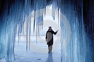 A woman looks at huge icicles in an ice cave. A journey on the frozen Lake Baikal in winter