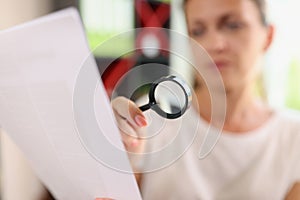 Woman looks through magnifying glass at document.