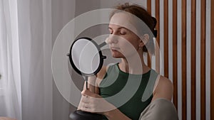 A woman looks in the mirror while grooming her skin, applying makeup