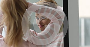 Woman looks in mirror, touch her hair enjoy morning routine