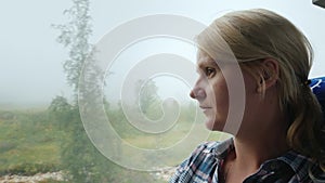 A woman looks out the window of a bus to a forest covered with thick fog. Traveling in Norway