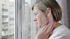 Woman looks out of window and touches painful spot on neck