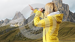 Woman looks at Passo Giau through binoculars pointing finger