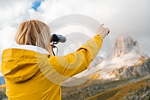 Woman looks at Passo Giau through binoculars pointing finger