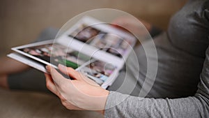 Woman looks at a photo book at home, lying on the sofa, close-up.Relaxed girl holding a photo book in the living room