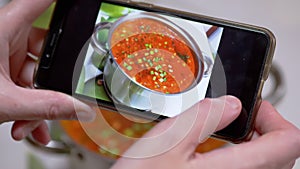 A Woman Looks at a Photo of Traditional Ukrainian Red Borscht on a Smartphone