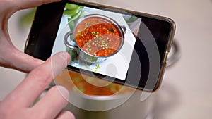 A Woman Looks at a Photo of Traditional Ukrainian Red Borscht on a Smartphone