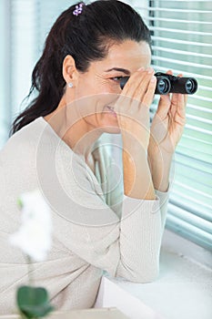 woman looks and searches with binoculars out window