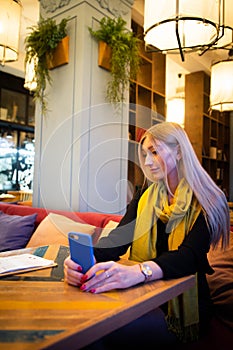 Woman looks at a smartphone in a cafe in the light of artificial cafe lamps