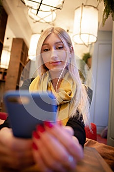 Woman looks at a smartphone in a cafe in the light of artificial cafe lamps