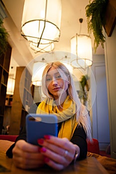 Woman looks at a smartphone in a cafe in the light of artificial cafe lamps