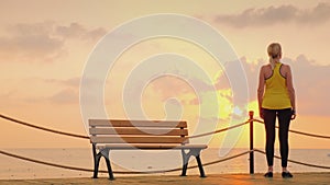 A woman looks at the sunrise against a beautiful dramatic sky. It stands on full length on a wooden pier.