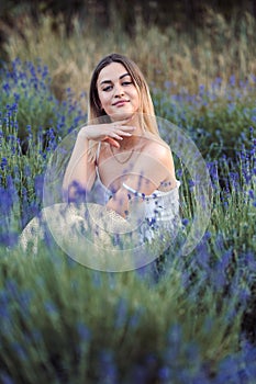 Woman Looks Tenderly at Camera Among Lavender, sits among lavender and enjoys flowering of lavender