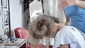 Woman looks to the mirror and enjoys her new style after making afro hairstyle at the beauty salon, smiling girl at the