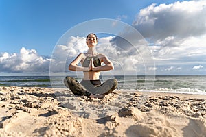 Woman in lotus position and namaste on beach. Girl enjoys meditation outdoors. Yoga harmony of soul and body healing