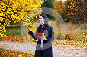 Woman with lowered protective mask walks in autumn park. Spending time at nature during coronavirus outbreak