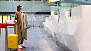 Woman with luggage stands at almost empty check-in counters at the airport terminal due to coronavirus pandemic