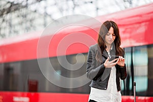 Woman with luggage at station traveling by train. Young tourist with cellphone and baggage on platform waiting for