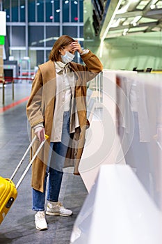 Woman with luggage upset over flight cancellation, stands at empty check-in counters at the airport terminal due to coronavirus