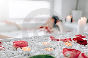 Woman lying in bath, rose petals, burning candles