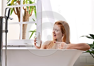 Woman lying in bathtub taking bath near open bathroom window and wash hand with soft shower gel cream lotion
