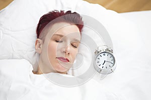 Woman lying in bed with alarm clock on pillow