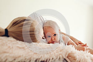 Woman lying on bed with her baby. Mother hugging kid. Family relaxing at home. Mother`s day